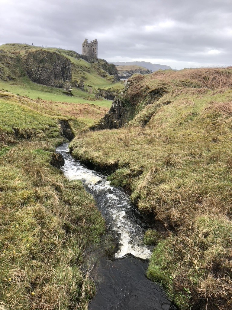 A small ruined castle in the background with a small stream in the foreground